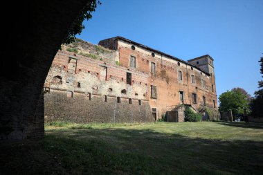 Terk edilmiş bir şatonun cephesi ve önünde bir çimen. Güneşli bir günde bir kemer tarafından çerçevelenmiş.