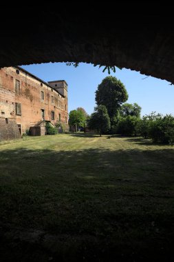 Terk edilmiş bir şatonun cephesi ve önünde bir çimen. Güneşli bir günde bir kemer tarafından çerçevelenmiş.