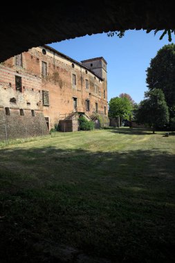 Terk edilmiş bir şatonun cephesi ve önünde bir çimen. Güneşli bir günde bir kemer tarafından çerçevelenmiş.