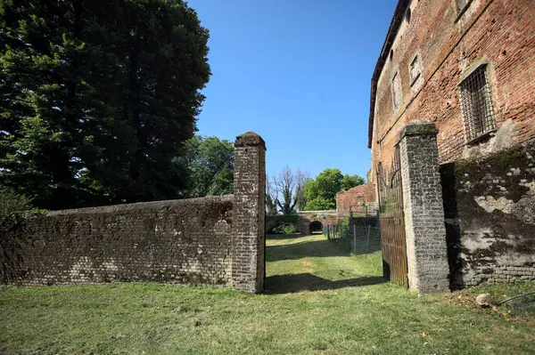 Bir şatonun kenarındaki patika, uzaktaki bir köprünün kemerlerinin altından geçiyor, yere düşen ağaçların gölgeleriyle.
