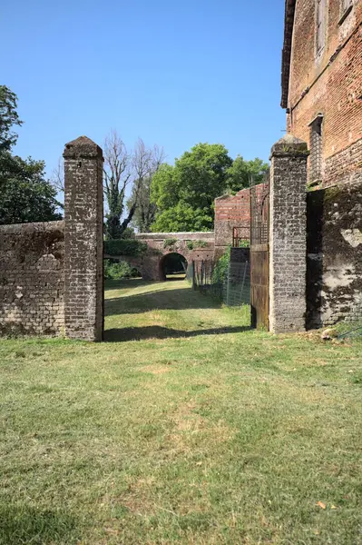 Bir şatonun kenarındaki patika, uzaktaki bir köprünün kemerlerinin altından geçiyor, yere düşen ağaçların gölgeleriyle.