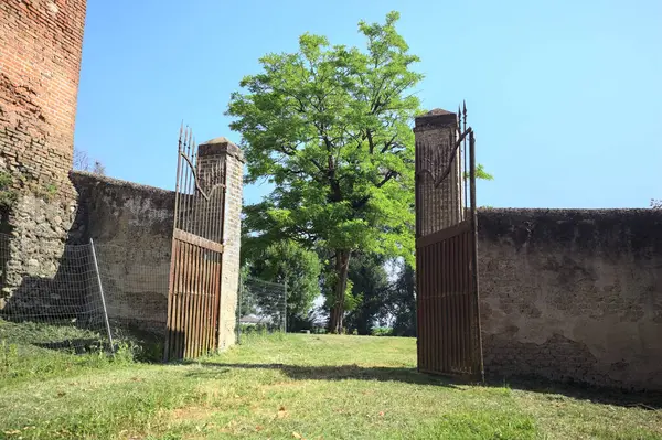 İtalya kırsalında güneşli bir günde, üzerinde ağaçlar olan bir çimenliğe açılan bir duvarın kapısını aç.