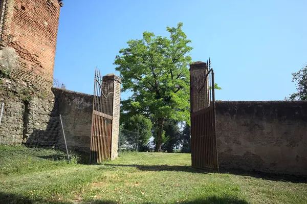 İtalya kırsalında güneşli bir günde, üzerinde ağaçlar olan bir çimenliğe açılan bir duvarın kapısını aç.