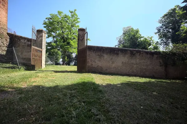 İtalya kırsalında güneşli bir günde, üzerinde ağaçlar olan bir çimenliğe açılan bir duvarın kapısını aç.