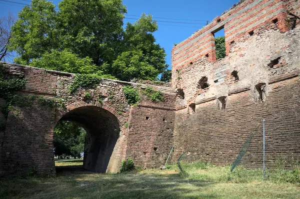 İtalya kırsalında güneşli bir günde terk edilmiş bir kalenin yanındaki tuğla köprünün altından geçen patika.