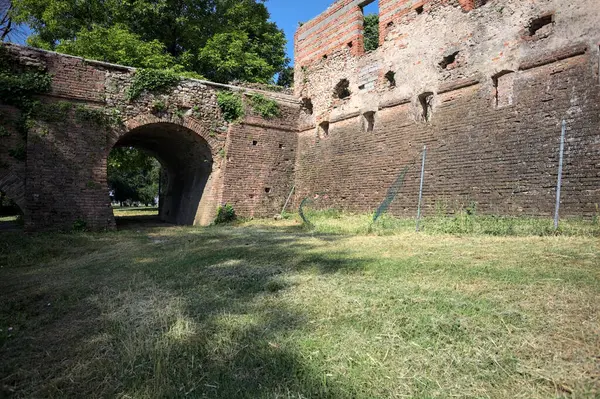 İtalya kırsalında güneşli bir günde terk edilmiş bir kalenin yanındaki tuğla köprünün altından geçen patika.