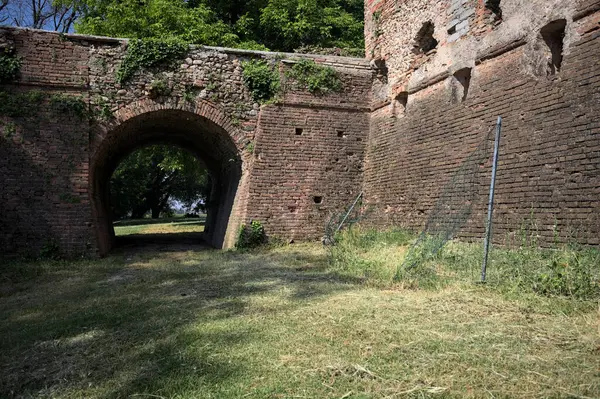İtalya kırsalında güneşli bir günde terk edilmiş bir kalenin yanındaki tuğla köprünün altından geçen patika.