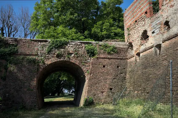 İtalya kırsalında güneşli bir günde terk edilmiş bir kalenin yanındaki tuğla köprünün altından geçen patika.