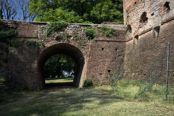 İtalya kırsalında güneşli bir günde terk edilmiş bir kalenin yanındaki tuğla köprünün altından geçen patika.