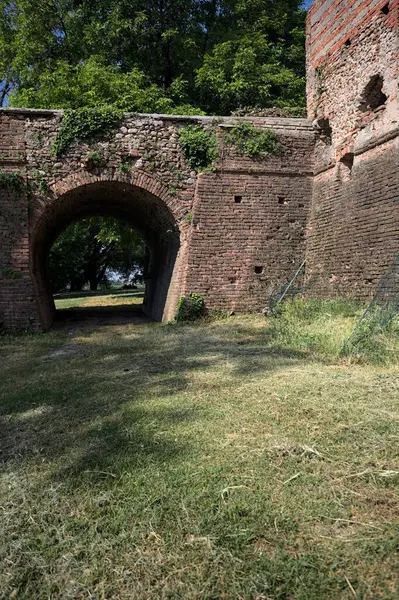 İtalya kırsalında güneşli bir günde terk edilmiş bir kalenin yanındaki tuğla köprünün altından geçen patika.
