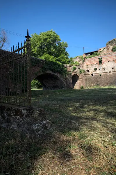 Terk edilmiş bir kalenin dış cephesi ve köprüsü güneşli bir günde İtalya kırsalında bir çitin arkasında görüldü.