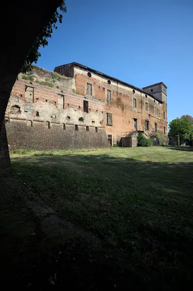 Terk edilmiş bir şatonun cephesi ve önünde bir çimen. Güneşli bir günde bir kemer tarafından çerçevelenmiş.