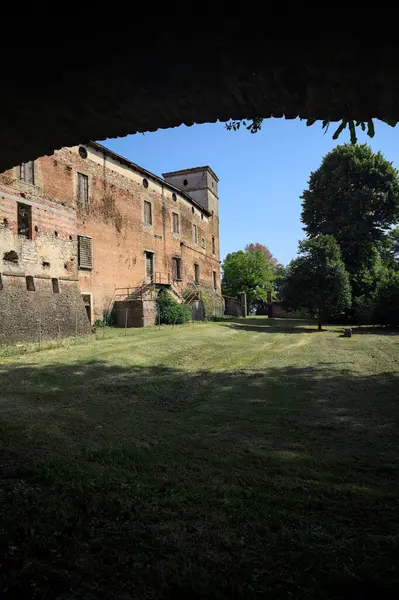 Terk edilmiş bir şatonun cephesi ve önünde bir çimen. Güneşli bir günde bir kemer tarafından çerçevelenmiş.