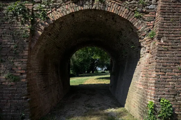 Ağaçlı bir çimenliğe uzanan köprünün kirişinin altındaki gölgedeki geçit.