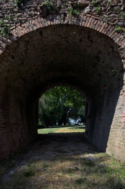 Ağaçlı bir çimenliğe uzanan köprünün kirişinin altındaki gölgedeki geçit.