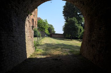 İtalya kırsalında güneşli bir günde terk edilmiş bir kalenin yanındaki tuğla köprünün altından geçen patika.