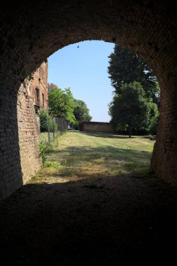 İtalya kırsalında güneşli bir günde terk edilmiş bir kalenin yanındaki tuğla köprünün altından geçen patika.