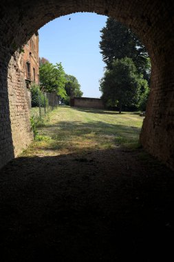 İtalya kırsalında güneşli bir günde terk edilmiş bir kalenin yanındaki tuğla köprünün altından geçen patika.