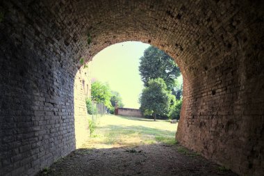 İtalya kırsalında güneşli bir günde terk edilmiş bir kalenin yanındaki tuğla köprünün altından geçen patika.
