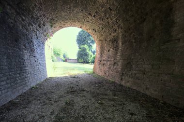 İtalya kırsalında güneşli bir günde terk edilmiş bir kalenin yanındaki tuğla köprünün altından geçen patika.