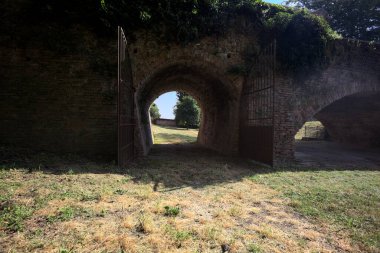 Üzerinde bitkiler büyüyen ve güneşli bir günde İtalyan kırsalında ağaçlarla çevrili tuğla köprü.