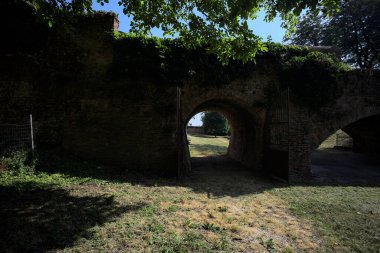 Üzerinde bitkiler büyüyen ve güneşli bir günde İtalyan kırsalında ağaçlarla çevrili tuğla köprü.