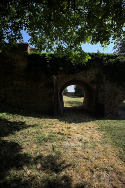 Üzerinde bitkiler büyüyen ve güneşli bir günde İtalyan kırsalında ağaçlarla çevrili tuğla köprü.