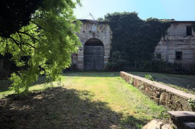 Güneşli bir günde, terk edilmiş bir kalenin ahşap kapısına çıkan kısa tuğla duvarlarla çevrili patika.