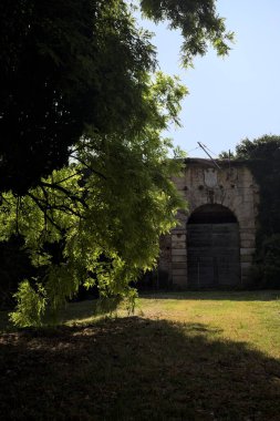 Güneşli bir günde, terk edilmiş bir kalenin ahşap kapısına çıkan kısa tuğla duvarlarla çevrili patika.