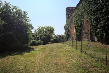 İtalya kırsalında güneşli bir günde ağaçlarla çevrili terk edilmiş bir kalenin yanındaki patikada.