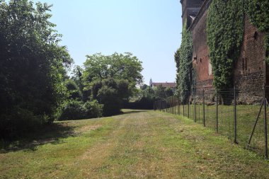 İtalya kırsalında güneşli bir günde ağaçlarla çevrili terk edilmiş bir kalenin yanındaki patikada.