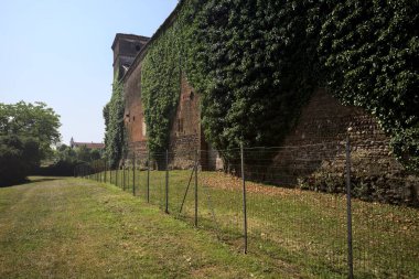 İtalya kırsalında güneşli bir günde ağaçlarla çevrili terk edilmiş bir kalenin yanındaki patikada.