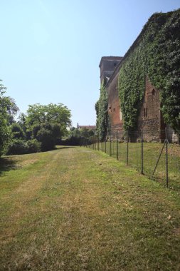 İtalya kırsalında güneşli bir günde ağaçlarla çevrili terk edilmiş bir kalenin yanındaki patikada.