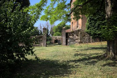 Güneşli bir günde, bir kalenin bahçesinde, ağaçların çerçevelediği ve çimenlikten görünen bir sınır duvarının kapısını aç.