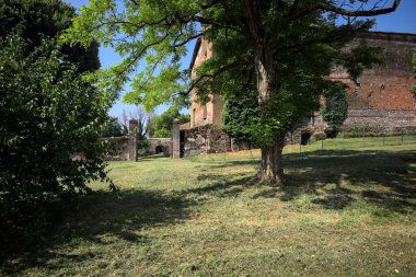 Güneşli bir günde, bir kalenin bahçesinde, ağaçların çerçevelediği ve çimenlikten görünen bir sınır duvarının kapısını aç.