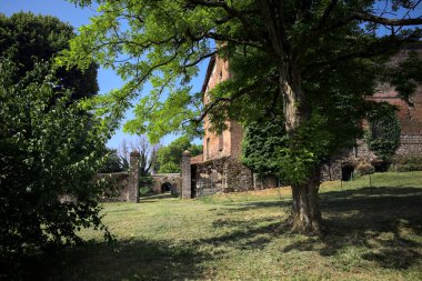 Güneşli bir günde, bir kalenin bahçesinde, ağaçların çerçevelediği ve çimenlikten görünen bir sınır duvarının kapısını aç.