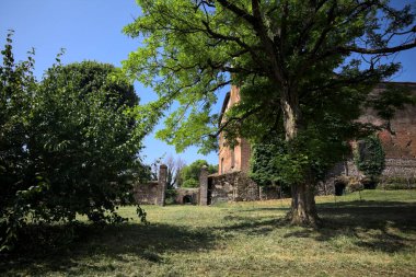 Güneşli bir günde, bir kalenin bahçesinde, ağaçların çerçevelediği ve çimenlikten görünen bir sınır duvarının kapısını aç.