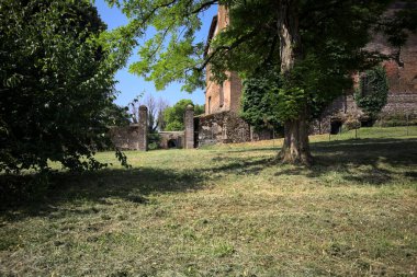 Güneşli bir günde, bir kalenin bahçesinde, ağaçların çerçevelediği ve çimenlikten görünen bir sınır duvarının kapısını aç.