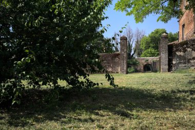 Güneşli bir günde, bir kalenin bahçesinde, ağaçların çerçevelediği ve çimenlikten görünen bir sınır duvarının kapısını aç.