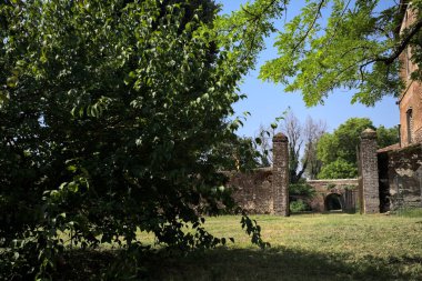 Güneşli bir günde, bir kalenin bahçesinde, ağaçların çerçevelediği ve çimenlikten görünen bir sınır duvarının kapısını aç.