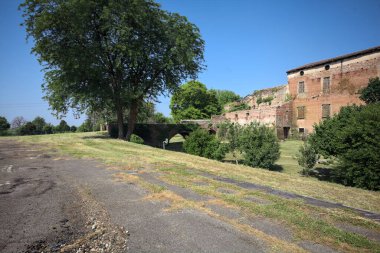 Kenarında kavak ağacı olan bir meydan ve arka planında ağaçlarla çevrili terk edilmiş bir saray İtalya kırsalında güneşli bir günde