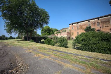 Kenarında kavak ağacı olan bir meydan ve arka planında ağaçlarla çevrili terk edilmiş bir saray İtalya kırsalında güneşli bir günde