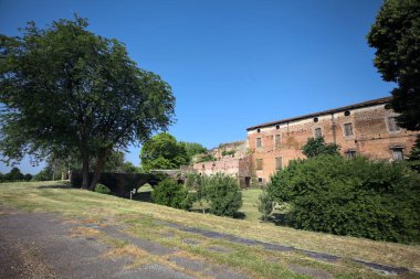 Kenarında kavak ağacı olan bir meydan ve arka planında ağaçlarla çevrili terk edilmiş bir saray İtalya kırsalında güneşli bir günde