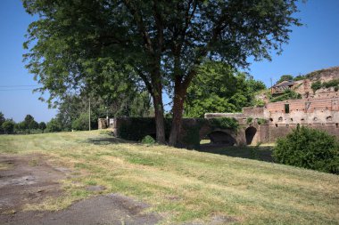 Kenarında kavak ağacı olan bir meydan ve arka planında ağaçlarla çevrili terk edilmiş bir saray İtalya kırsalında güneşli bir günde