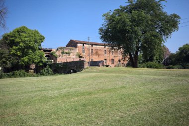 Kenarında kavak ağacı olan bir meydan ve arka planında ağaçlarla çevrili terk edilmiş bir saray İtalya kırsalında güneşli bir günde
