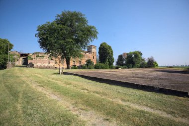 Kenarında kavak ağacı olan bir meydan ve arka planında ağaçlarla çevrili terk edilmiş bir saray İtalya kırsalında güneşli bir günde