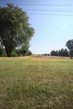 İtalya 'nın kırsal kesimlerinde güneşli bir günde bitkilerden yapılmış bir çitin arkasında ufka kadar uzanan bir mısır tarlası olan ağaçlarla çevrili beton kare.