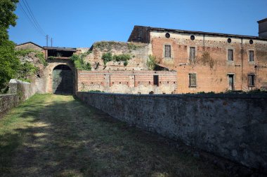 Güneşli bir günde, İtalya 'da terk edilmiş bir sarayın kapısındaki ahşap kapıya uzanan çimlerle kaplı tuğla köprü.