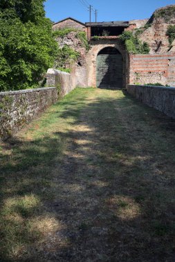 Güneşli bir günde, İtalya 'da terk edilmiş bir sarayın kapısındaki ahşap kapıya uzanan çimlerle kaplı tuğla köprü.