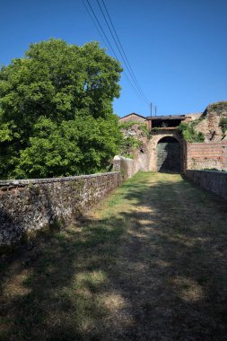 Güneşli bir günde, İtalya 'da terk edilmiş bir sarayın kapısındaki ahşap kapıya uzanan çimlerle kaplı tuğla köprü.
